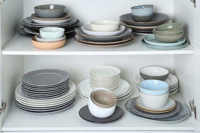 Photo of Different clean plates and bowls on shelves in cabinet