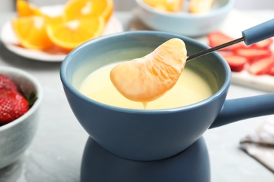 Dipping tangerine segment into pot with white chocolate fondue on table, closeup