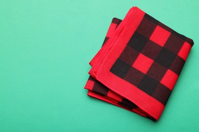 Folded red checkered bandana on turquoise background, top view. Space for text