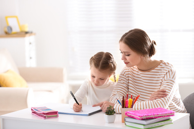 Woman helping her daughter with homework at table indoors