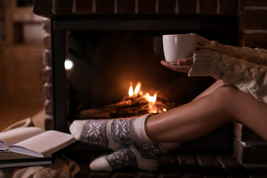 Photo of Woman with cup of hot cocoa near fireplace indoors, closeup