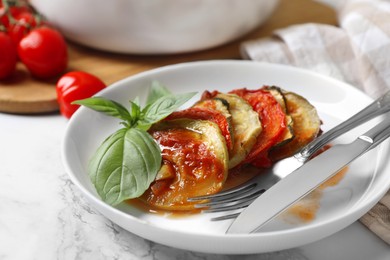 Photo of Delicious ratatouille served with basil on white marble table, closeup