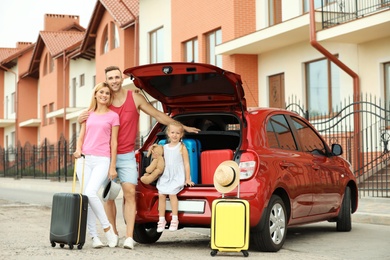 Happy family near car trunk with suitcases outdoors