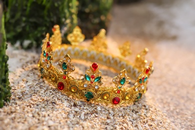 Beautiful golden crown on sand outdoors, closeup. Fantasy item