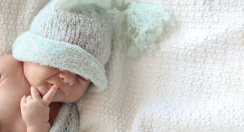 Cute newborn baby in warm hat lying on white plaid, top view with space for text. Banner design