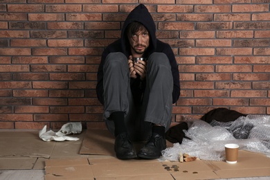 Poor man sitting with mug on floor near brick wall