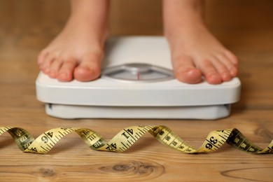 Photo of Overweight girl using scales near measuring tape on wooden floor, selective focus