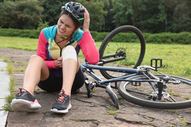 Young woman with injured knee near bicycle outdoors