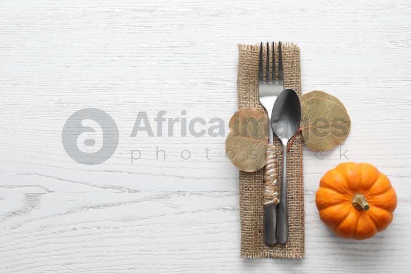 Cutlery with leaves, pumpkin and space for text on white wooden background, flat lay. Table setting elements
