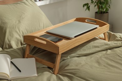 Wooden tray with modern laptop and smartphone on bed indoors