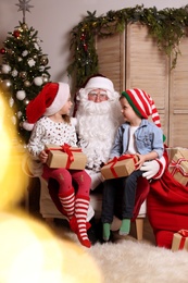 Santa Claus and little children with presents in room decorated for Christmas