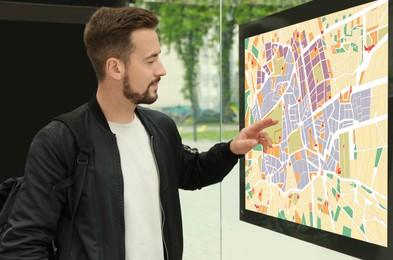 Young man with backpack near public transport map at bus stop