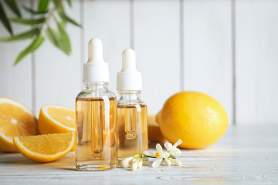 Bottles of citrus essential oil, flower and lemons on white wooden table. Space for text