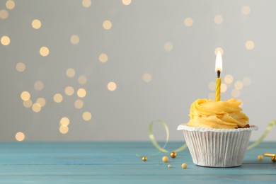 Tasty birthday cupcake on light blue wooden table against blurred lights. Space for text