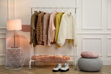 Rack with stylish warm clothes and shoes in modern dressing room