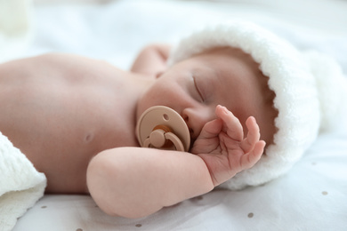 Cute newborn baby in white knitted hat sleeping on bed, closeup
