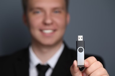 Man with usb flash drive against grey background, focus on device. Space for text