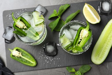 Photo of Spicy cocktail with jalapeno, cucumber and lime on black table, flat lay