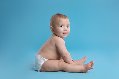Cute baby in dry soft diaper sitting on light blue background