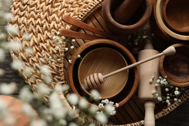 Photo of Wooden bowls, rolling pin and honey dipper near flowers on wicker mat, flat lay