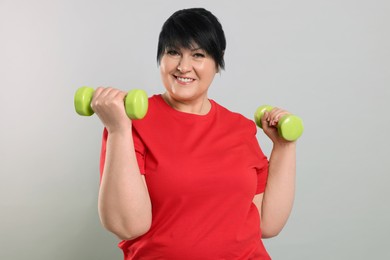 Photo of Happy overweight mature woman doing exercise with dumbbells on grey background