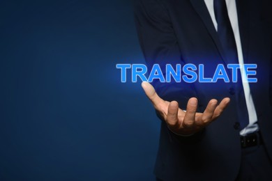 Man showing virtual model of word TRANSLATE against dark blue background, closeup. Space for text
