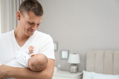 Happy father holding his cute baby at home, space for text