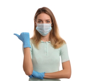 Young woman in medical gloves and protective mask pointing thumb aside on white background