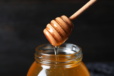 Jar of organic honey and dipper on dark background, closeup
