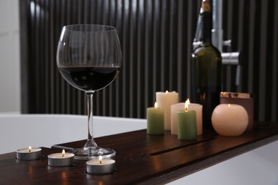 Glass of tasty red wine and burning candles on bathtub tray