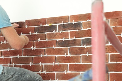 Professional builder gluing decorative brick on wall, closeup. Tiles installation process