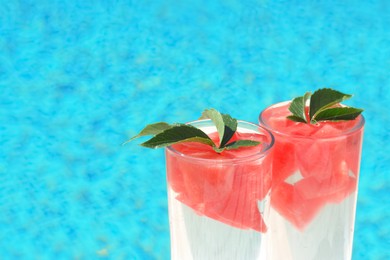 Refreshing watermelon drink in glasses near swimming pool outdoors, closeup. Space for text