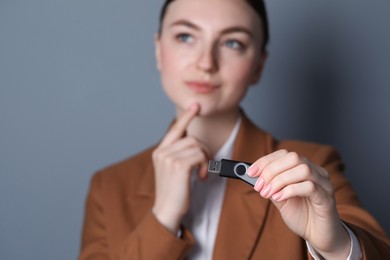 Photo of Woman holding usb flash drive against grey background, focus on hand