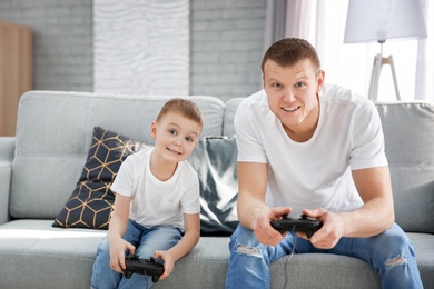 Happy dad and his son playing video games at home. Father's day celebration