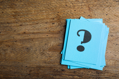 Blue paper cards with question mark on wooden background, top view. Space for text
