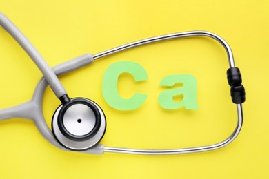 Photo of Stethoscope and calcium symbol made of green letters on yellow background, flat lay