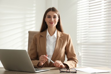 Portrait of beautiful young businesswoman with laptop at table in office