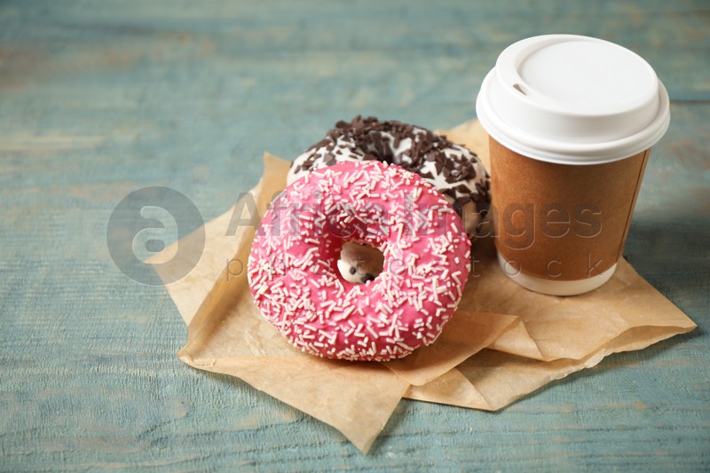 Yummy donuts with sprinkles and paper cup on wooden table