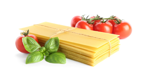 Uncooked lasagna sheets, tomatoes and basil on white background