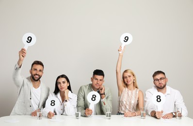 Panel of judges holding different score signs at table on beige background