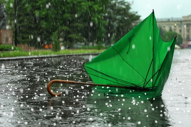 Broken green umbrella in park on rainy day with hail