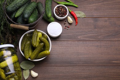 Photo of Bowl of pickled cucumbers and ingredients on wooden table, flat lay. Space for text