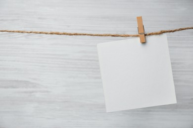 Clothespin with blank notepaper on twine against white wooden background. Space for text