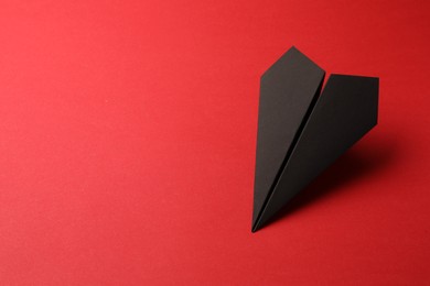 Photo of Handmade black paper plane on red background, space for text