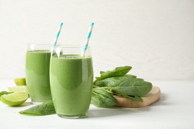 Glasses of healthy green smoothie with fresh spinach on white wooden table against light background. Space for text