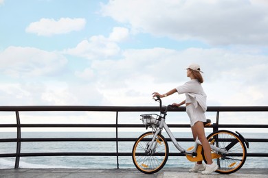 Beautiful young woman with bicycle near sea. Space for text