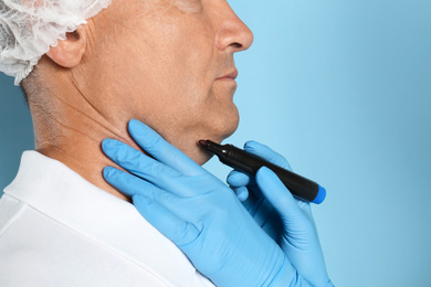 Surgeon with marker preparing man for operation against blue background, closeup. Double chin removal