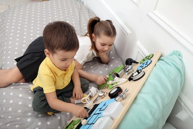 Little boy and girl playing with busy board on bed indoors