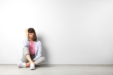 Unhappy young girl sitting on floor near white wall. Space for text