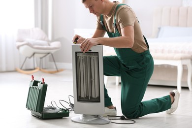 Professional technician repairing electric ultrared heater with screwdriver indoors